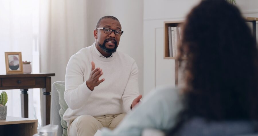 A black male therapist is talking with his patient in office.